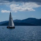 sailboat on blue waters with clouds and dark blue mountains in the background