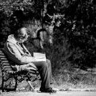 black and white photograph of old man sitting on park bench reading