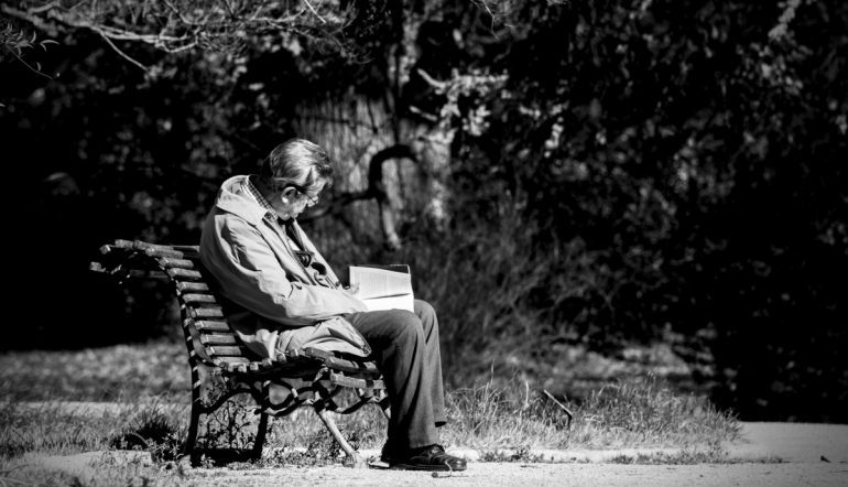 black and white photograph of old man sitting on park bench reading