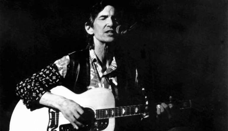 Townes Van Zandt with a guitar, singing into a microphone