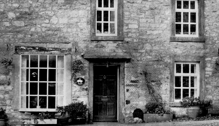 black and white photograph of the front of a cottage - door, windows, stone wall