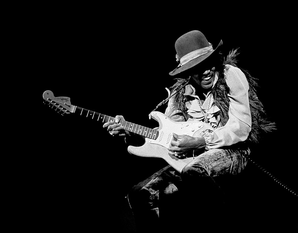 Black and white photo of Jimi Hendrix playing the guitar on stage.