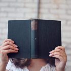 Image of a girl reading a book which covers her face.