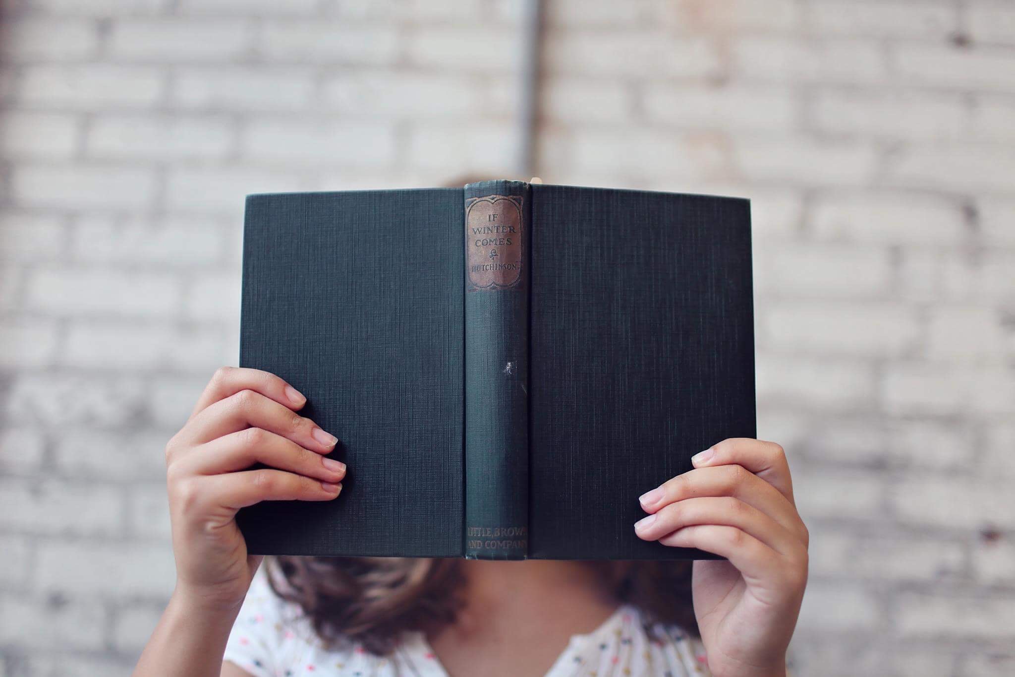 Image of a girl reading a book which covers her face.