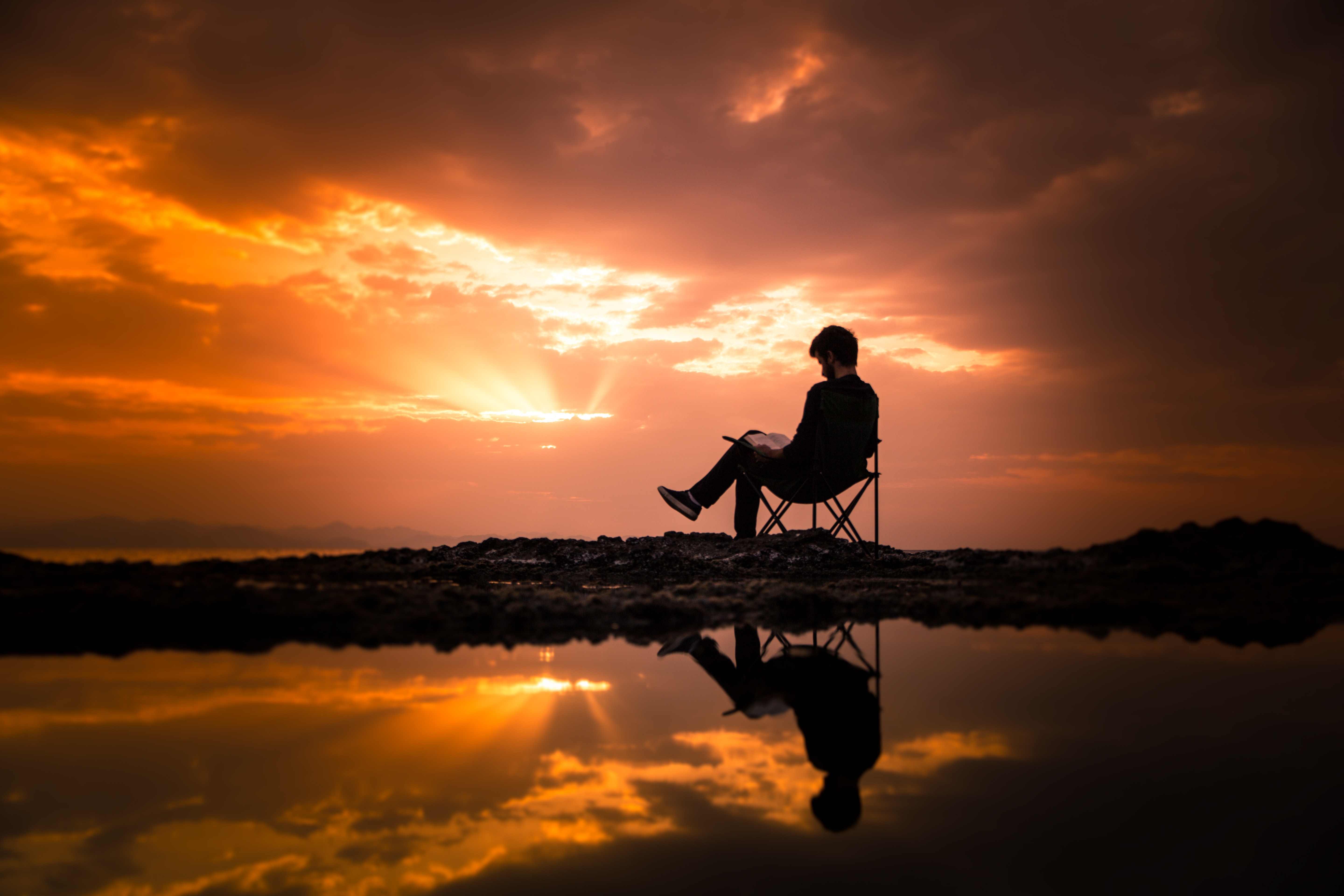 Image of a man sitting, reading a book outside during a sunset
