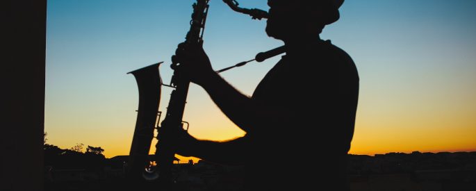 Photograph of a saxophone player silhouetted against a blue and orange sky
