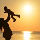 Photograph of the silhouette of a mother holding her child at the beach