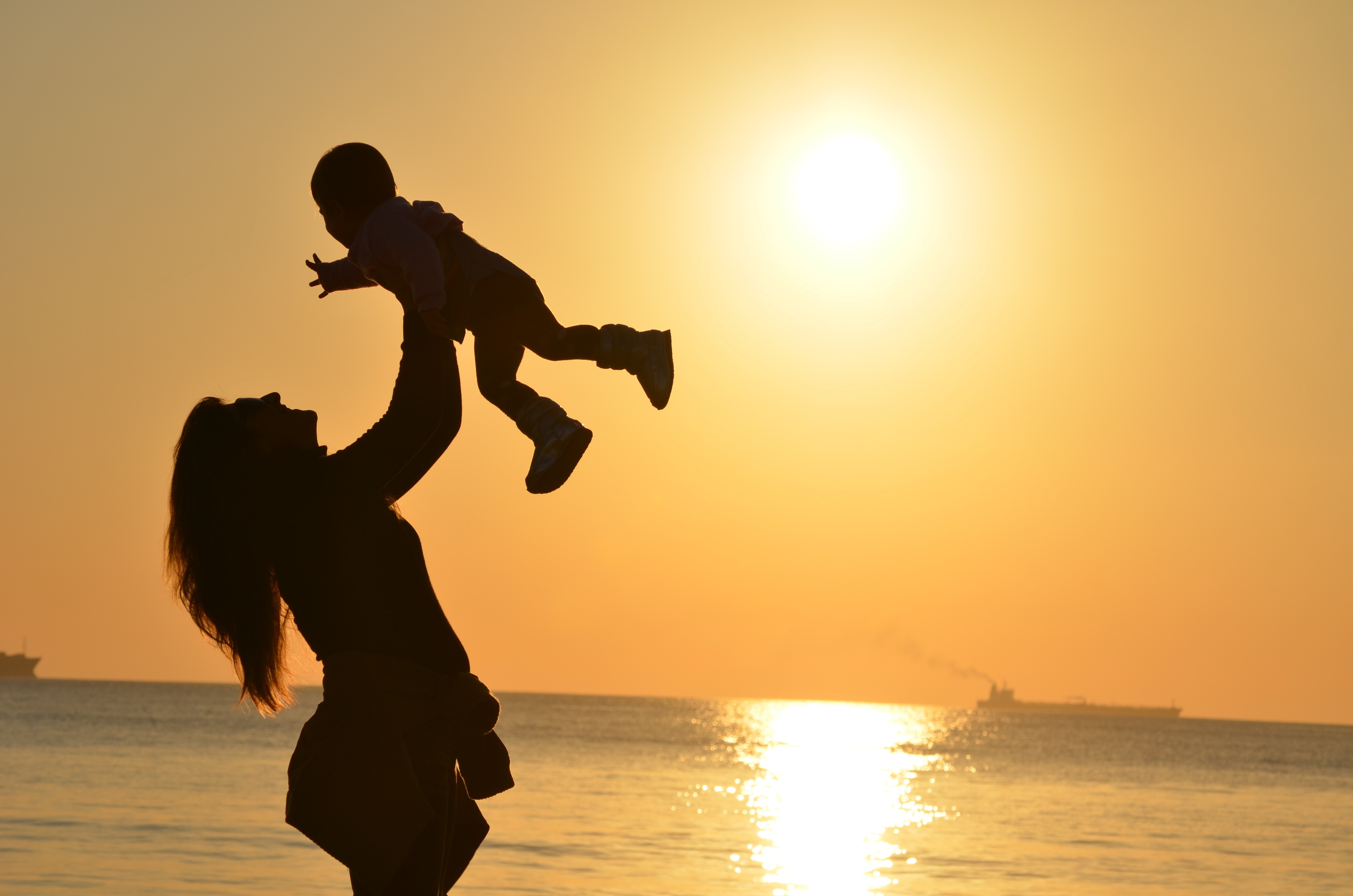 Photograph of the silhouette of a mother holding her child at the beach