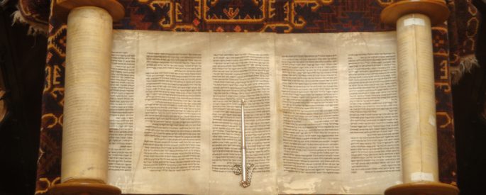 Photograph of an old Torah scroll open and resting on a wooden table
