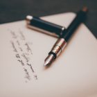 A black fountain pen sits atop a half-written letter.