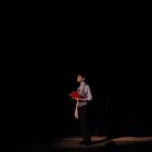 a young person on a stage is in the spotlight, reading from a red book