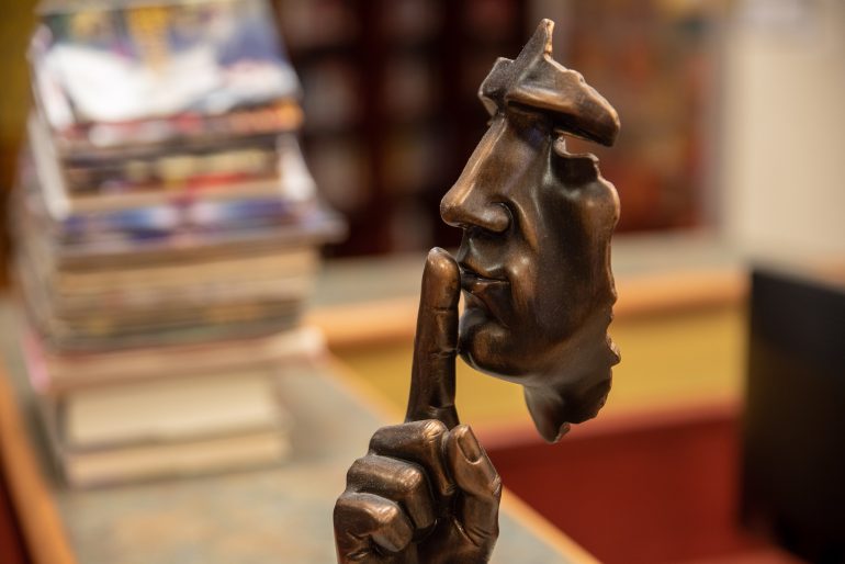 experimental copper statue of a man's face with a finger over its lips in "hushing" motion