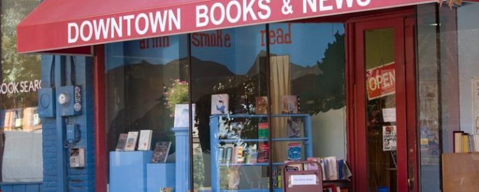 photo of the front of a bookstore with a sign on an overhang that reads "Downtown Books & News"