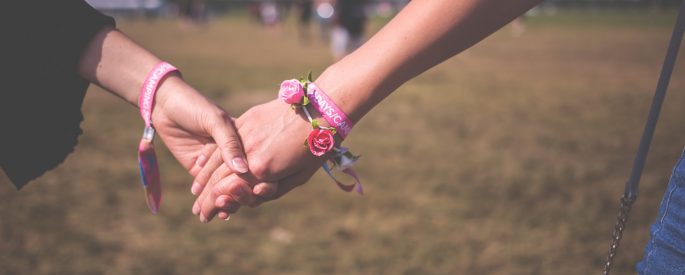 Two people holding hands wearing the same bracelets, one wears a bracelet made of small, fake roses