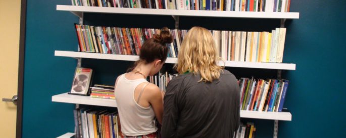 photo of two girls with their backs to the camera looking at a full bookshelf