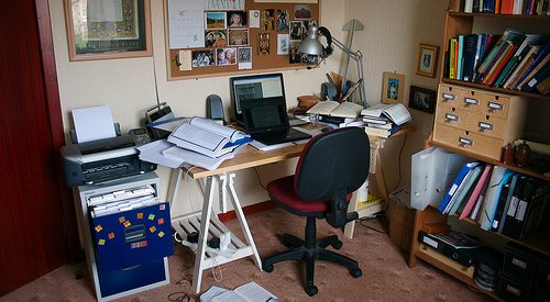 photo of a cluttered desk space with a mini fridge, an open laptop, and a cork board hanging above the desk
