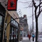 photo of the front of a cafe on a snowy city street, there is a red sign hanging outside the storefront that reads "caffe art java"