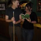 photo of two people standing together, one holding a pool cue, the other holding a book