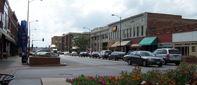 photo of the downtown of Columbia Missouri which feature many cars parked outside a brick storefront street