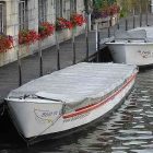 photograph of a canal in Belgium, where a few, small boats docked next to a building accented with small flowerboxes