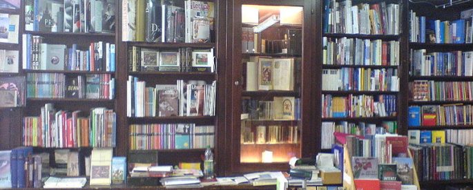 photograph of a bookstore with a multitude of tall floor-to-ceiling shelves and stacks of books