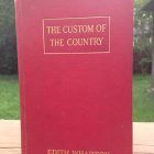 the Custom of the Country by edith wharton has been propped up to stand on top of a picnic bench