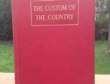 the Custom of the Country by edith wharton has been propped up to stand on top of a picnic bench