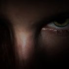 A white person with green eyes stares out of the shadows.