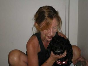 The image shows a tan woman smiling and holding a black, fluffy dog