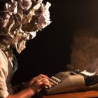 Photo of a man at a typewriter with a crumpled piece of paper as a head and more crumpled papers scattered around him