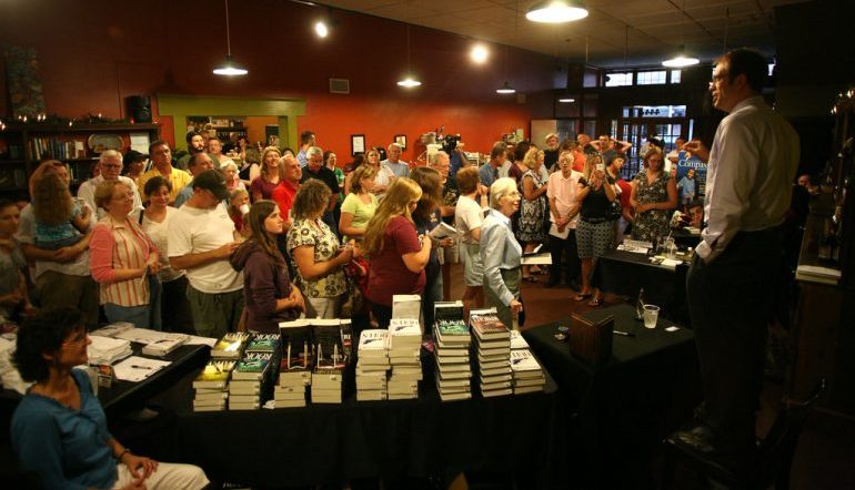 Crowd of people in bookstore with stacks of books to buy