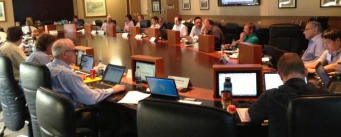 Group of people sitting around a conference table with laptops