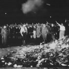 Black and white photo of a group of people burning a pile of books in the middle