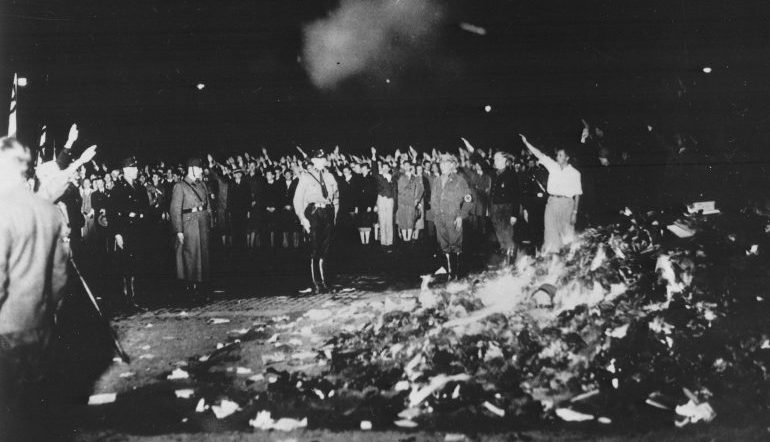 Black and white photo of a group of people burning a pile of books in the middle