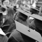 A black and white photo of people sitting with graduation caps on.