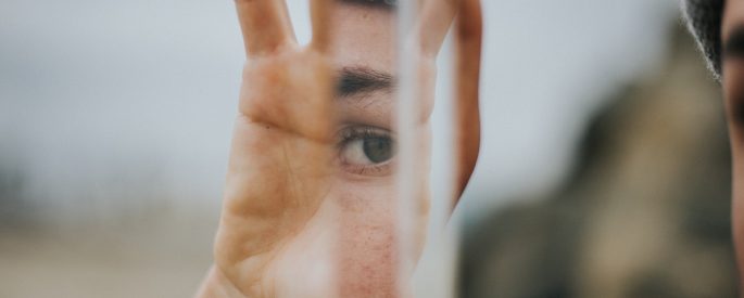 A person holds a piece of glass up which reflects their face in it.