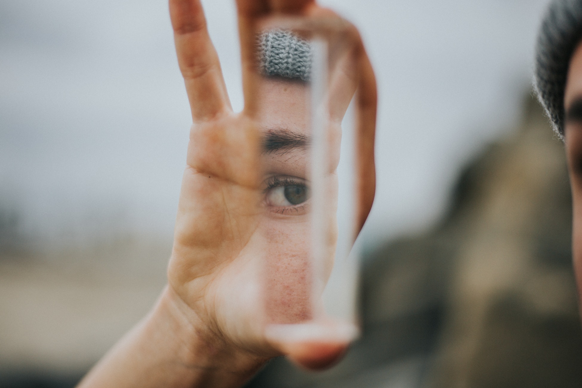 A person holds a piece of glass up which reflects their face in it.
