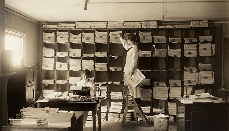 Woman sorting papers in boxes in old publishing company