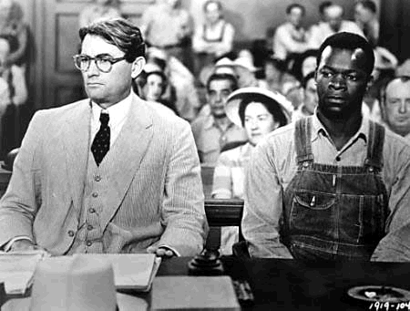 Black and white still from a movie scene of a white man in a suit sitting next to a Black man in a court room