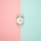silver bell alarm clock on pink and blue wall