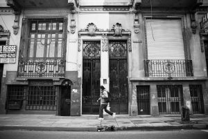 Black and white picture of a person walking in front of some buildings. 