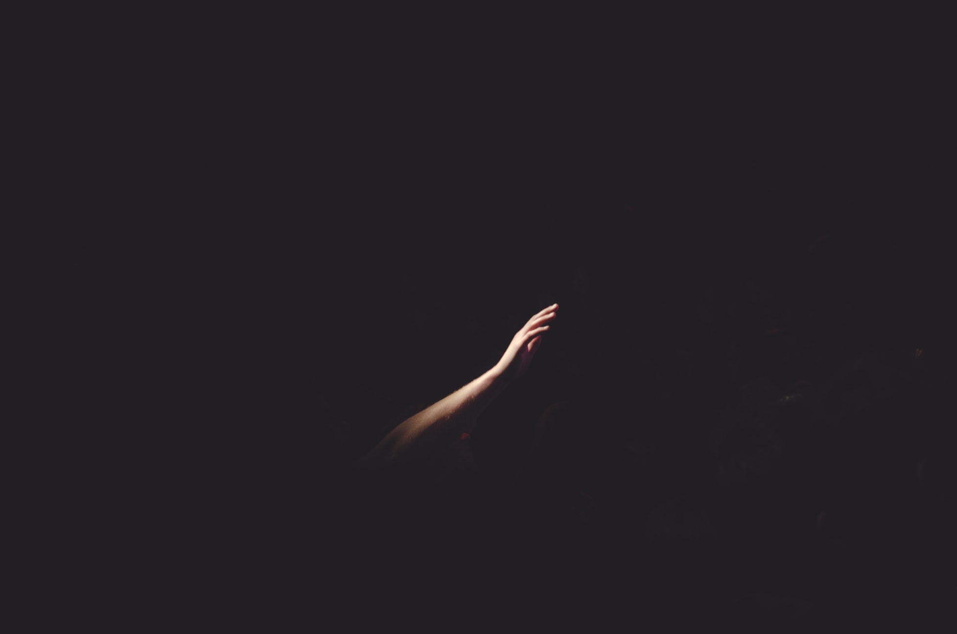 Picture of a right human hand reaching through the darkness. 
