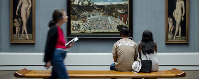 man and woman sitting on bench while looking at painting