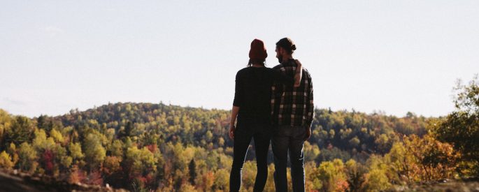 couple standing in front green trees field