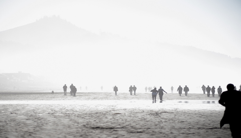 Several people walking towards mountains surrounded by fog.
