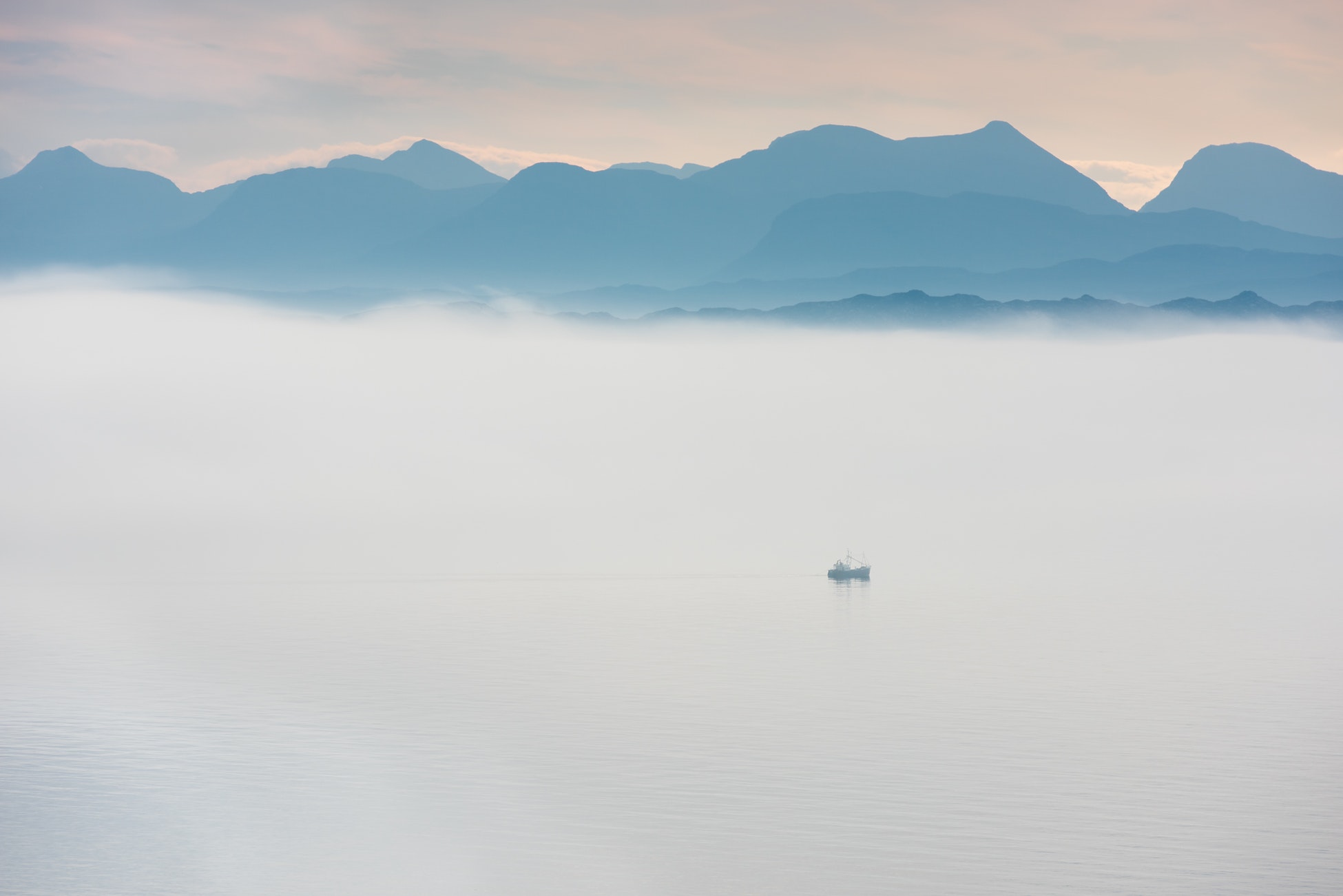 Small boat on large open water surrounded by mountains and fog.