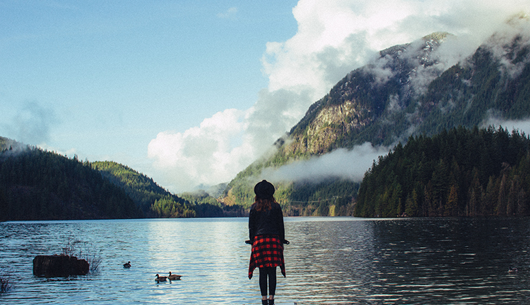 Woman standing in front of a lake and a large mountain.