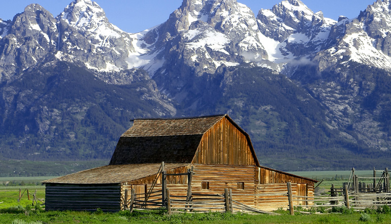 small wooden barn in front of snow-topped mountain range 