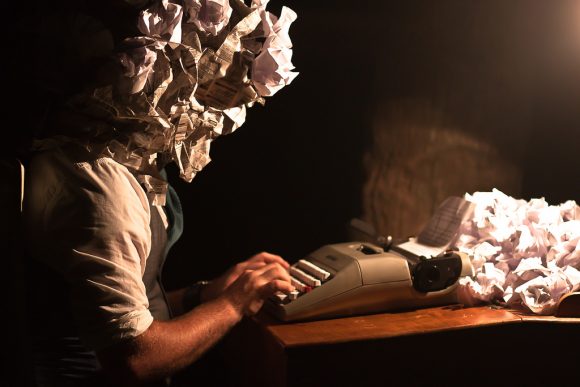 A person sitting at a typewriter with crumpled paper on the desk in front of them. Their head is also replaced with crumpled paper.