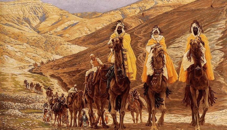 Three people dressed in yellow robes riding on camels and leading others through desert mountains.